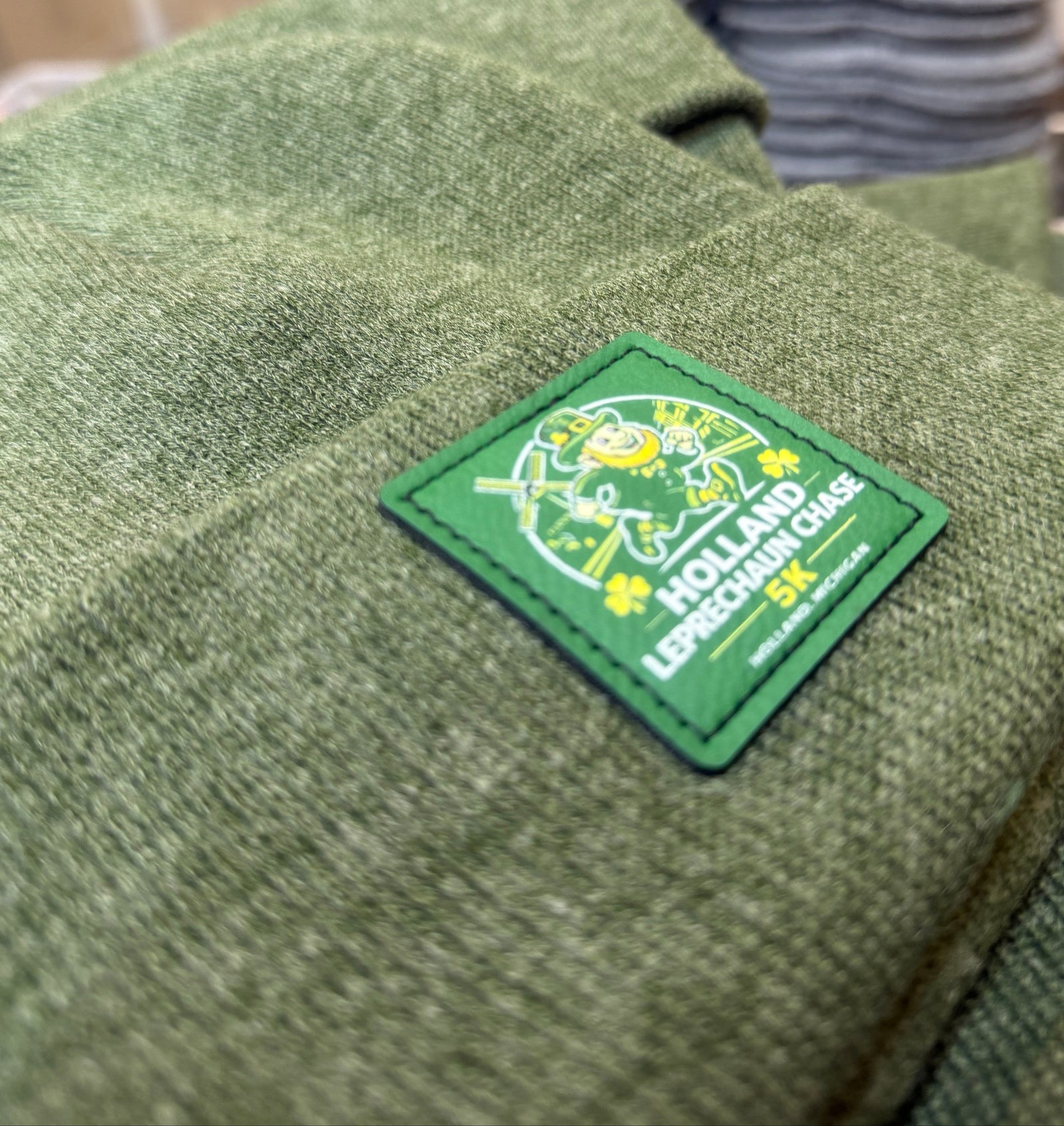 Green beanie made in USA with a patch featuring text and graphics. Showing how UV custom print on a custom beanie made in USA looks like. 