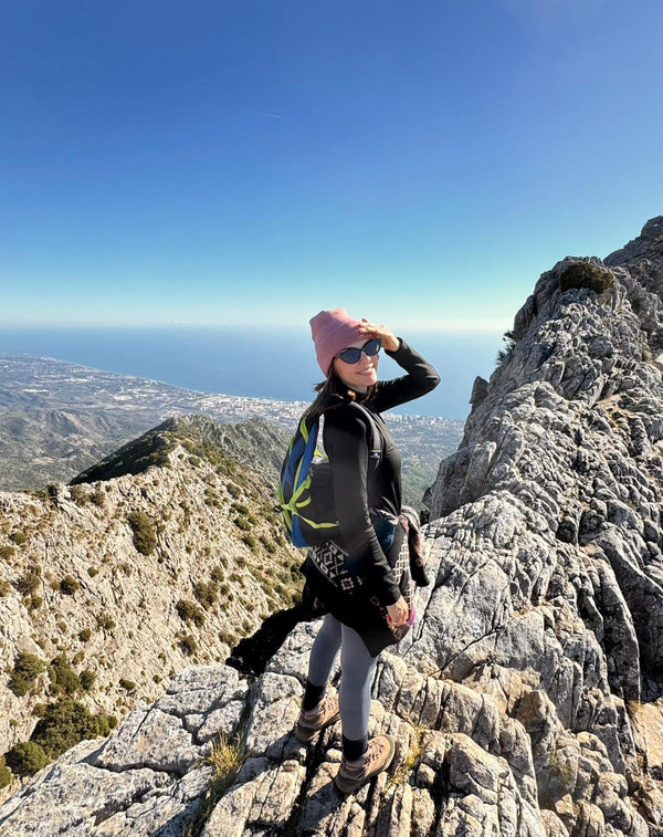 Person standing on a mountain peak with a scenic view of the ocean and sky.